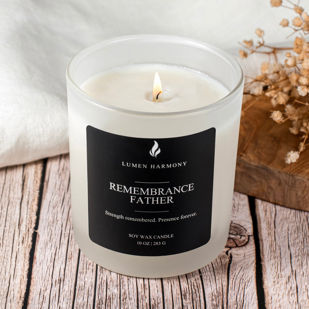 Lumen  Harmony candle labeled 'Remembrance Father' on a wooden surface with dried flowers.
