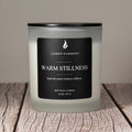 Lumen Harmony candle labeled 'Warm Stillness' on a wooden surface with a neutral background
