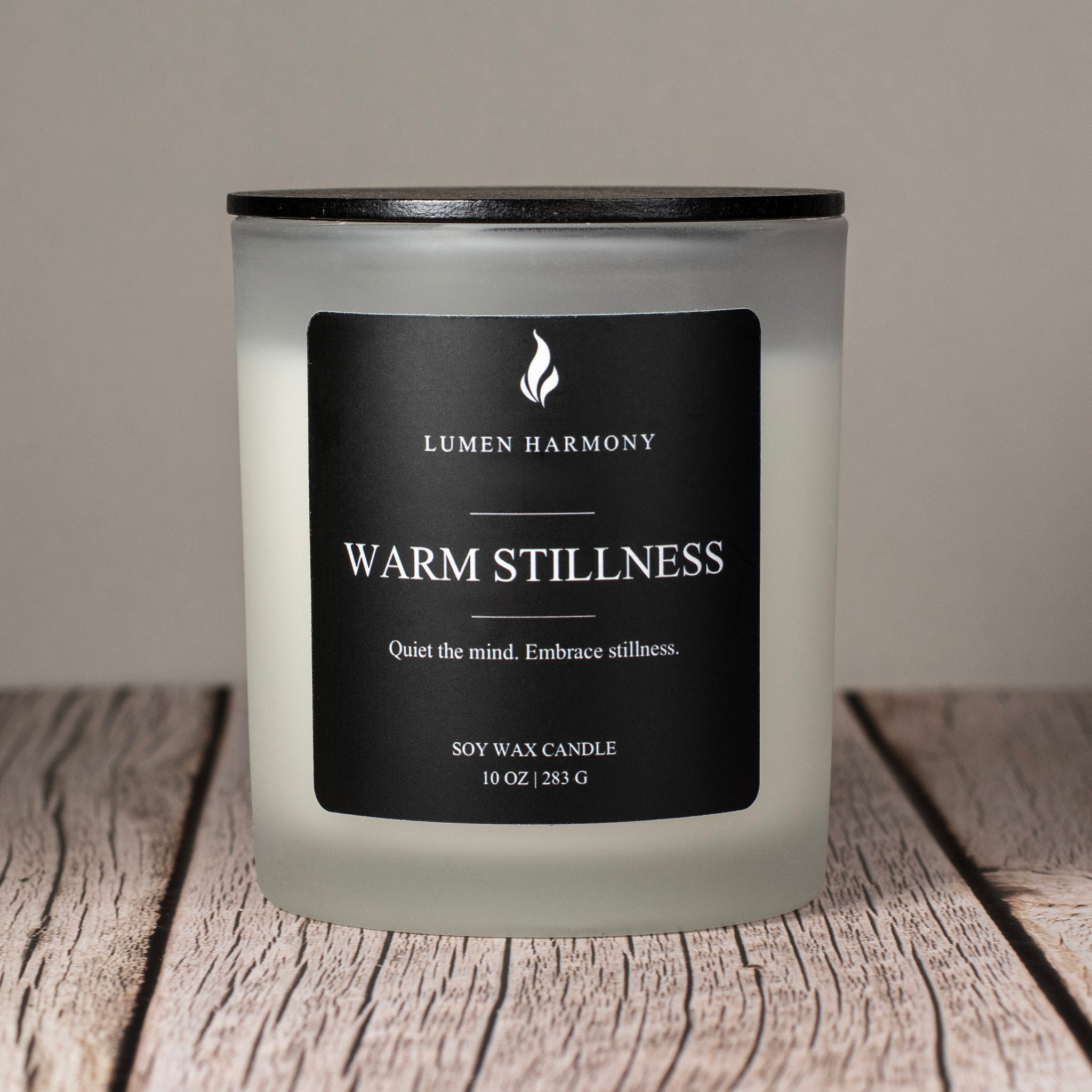 Lumen Harmony candle labeled 'Warm Stillness' on a wooden surface with a neutral background