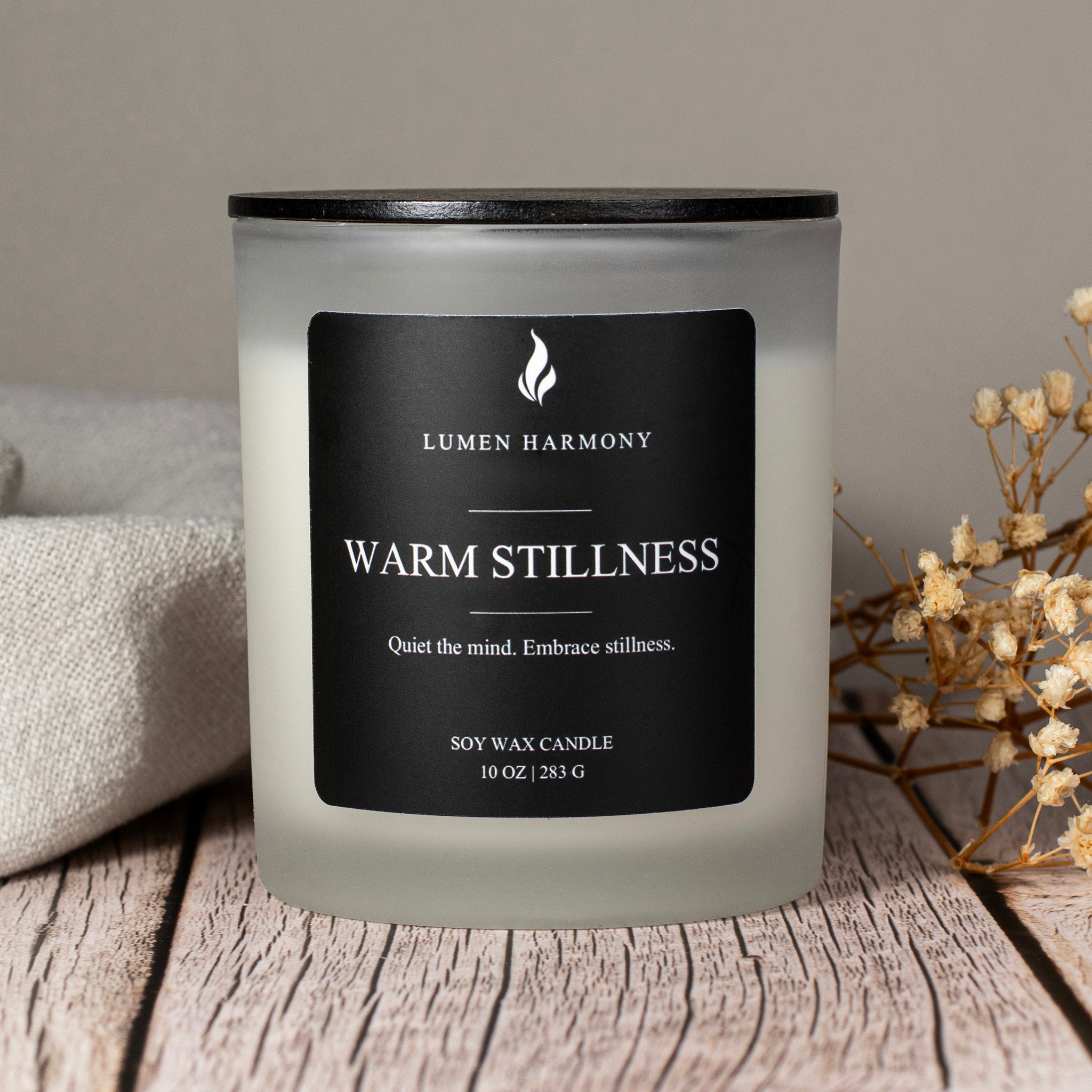 Lumen Harmony candle labeled 'Warm Stillness' on a wooden surface with a neutral background.